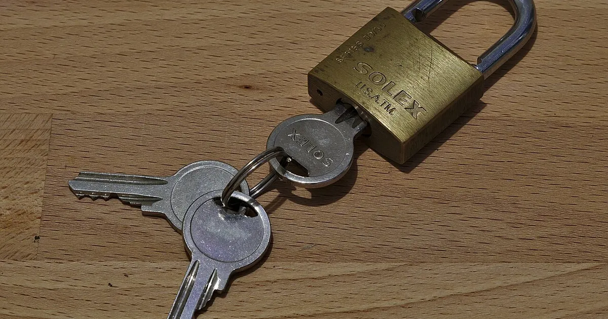 A brass padlock with its keys on a wooden table